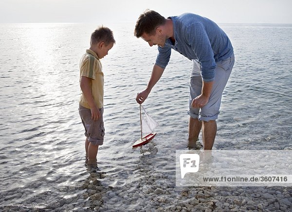 Vater und Sohn mit Spielzeugboot am Strand