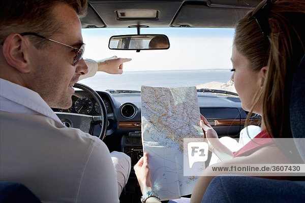 Couple looking at map in car by sea