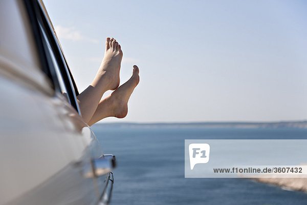Woman stretching feet from car by sea