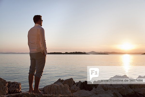 Mann beobachtet Sonnenuntergang am felsigen Strand
