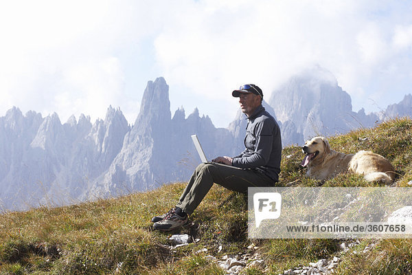 Man and dog in mountains with laptop