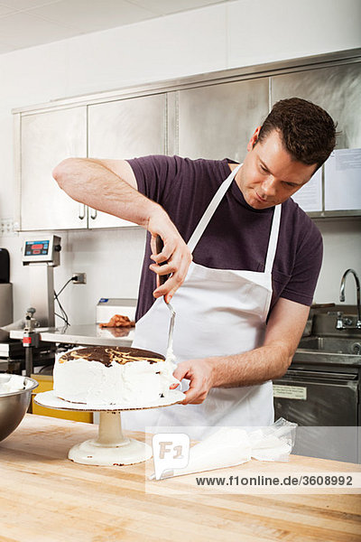 Männlicher Koch  der einen Kuchen in der Großküche glasiert