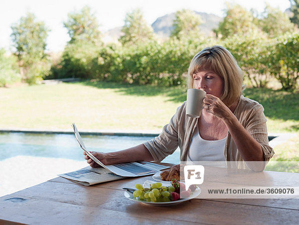 Woman outdoors  reading newspaper and drinking coffee