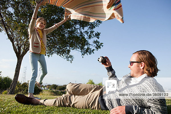 Young man photographing girlfriend as she shakes out a blanket