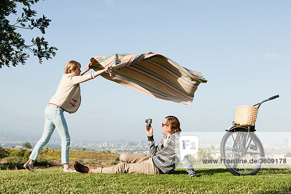 Young man photographing girlfriend as she shakes out a blanket
