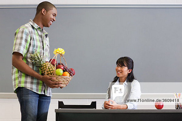 Ein männlicher Gymnasiast gibt dem Lehrer einen Korb mit Früchten.