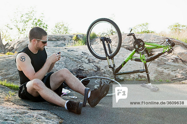Männlicher Radfahrer  der einen Reifen mit Reifenpannen repariert