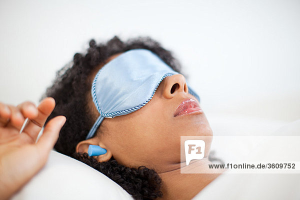 Frau schläft in Augenmaske und Ohrstöpseln