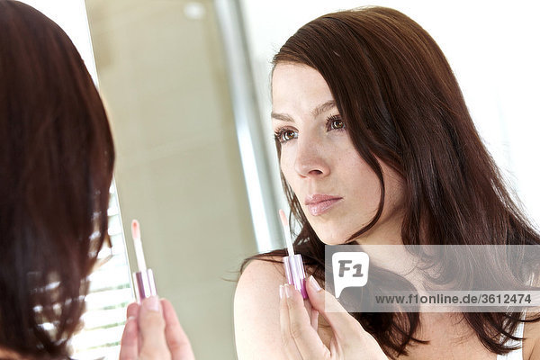 Frau im Badezimmer trägt Lipgloss auf