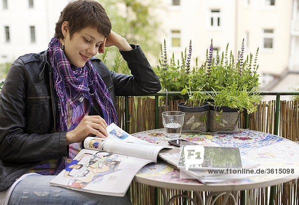 Junge Frau liest eine Zeitschrift auf dem Balkon