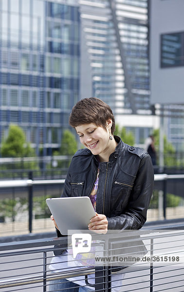 Junge Frau benutzt einen iPad vor einem Bürogebäude