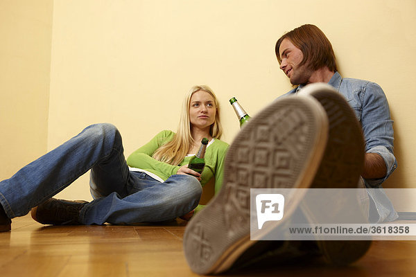 Junges Paar sitzt auf dem Fußboden und trinkt Bier