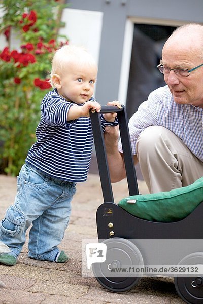 Grandfather and toddler with doll's pram outdoors