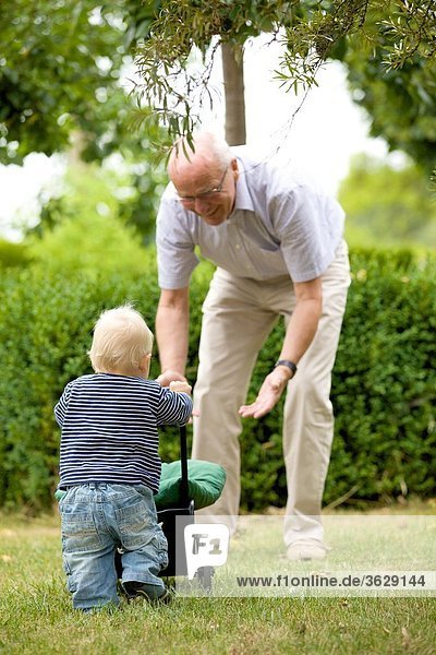 Großvater und Kleinkind mit Puppenwagen im Freien