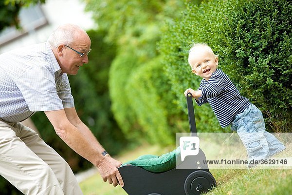 Großvater und Kleinkind mit Puppenwagen im Freien