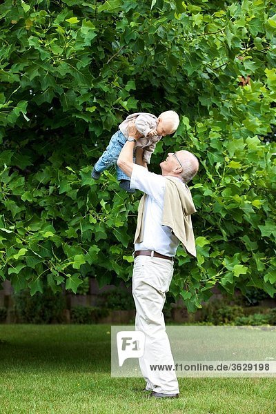 Großvater hebt Kleinkind im Freien hoch