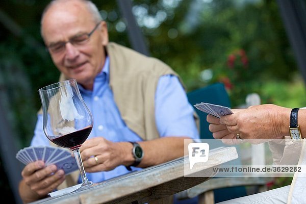 Seniorenpaar spielt Karten und trinkt Rotwein