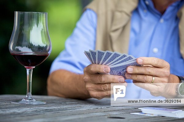 Senior spielt Karten und trinkt Rotwein  close-up