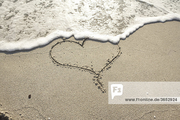 Herz-Symbol in nassem Sandstrand wird von Welle fortgespült