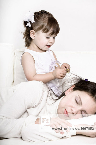 Kleines Mädchen spielt mit dem Haar der schlafenden Mutter
