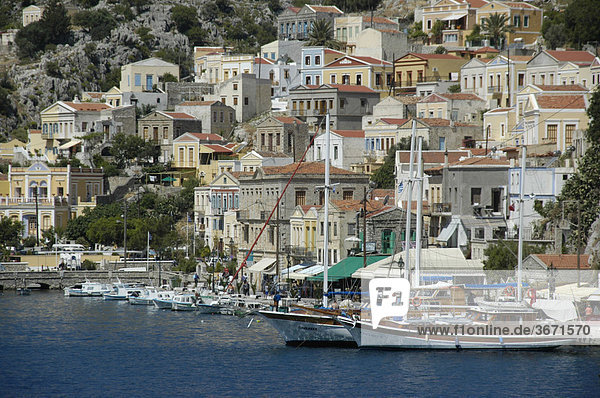 Blick auf die farbenfrohen ockerfarbenen Häuser mit Segelbooten im Hafen der Insel Symi Griechenland
