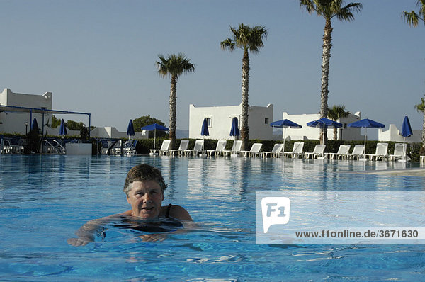 Active seniors woman is swimming in the water of the pool with palm trees in the back Hotel Aeolos Beach Island of Kos Greece