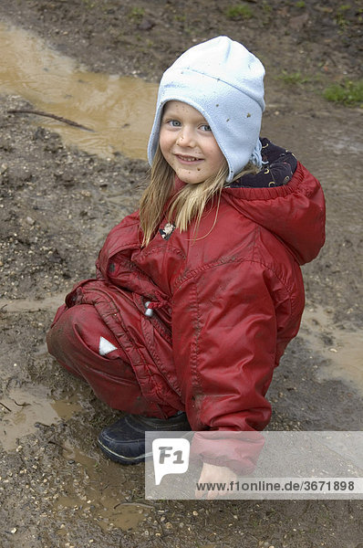 Kind spielt bei schlechtem Wetter im Regen in Pfützen und im Matsch Schlamm