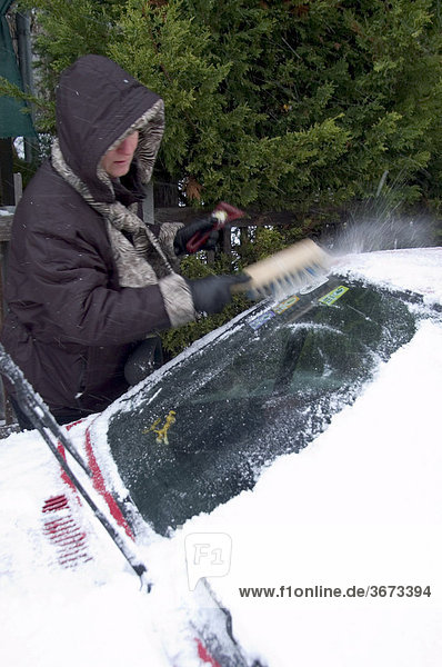 Woman removes snow and ice from a car