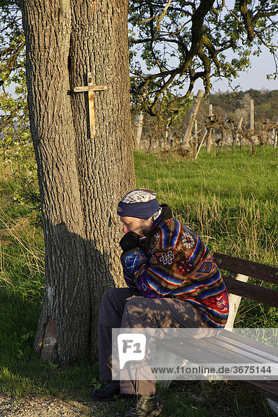 Mann auf Bank unter Baum mit Kreuz bei Großau bei Bad Vöslau Niederösterreich Österreich