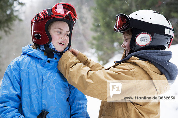 Young boy helping girl do up ski helmet