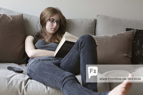 Young woman reading book on sofa