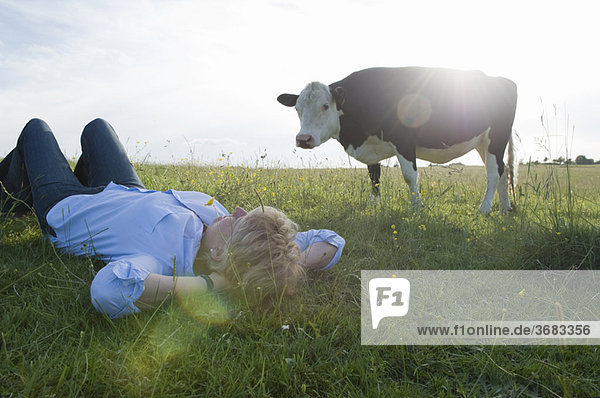 Frau entspannt im Feld mit Kuh