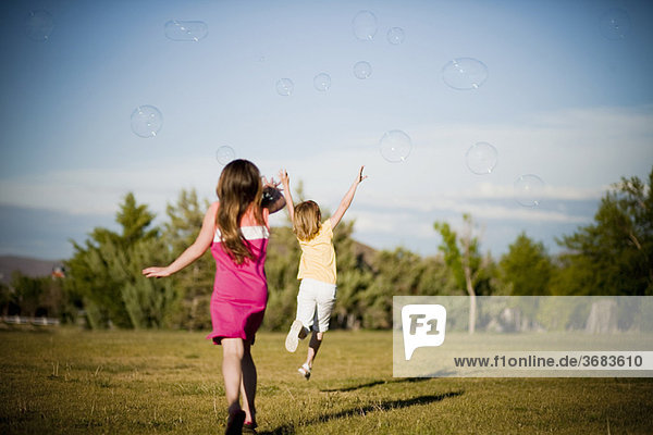 2 young girls chasing bubbles in park
