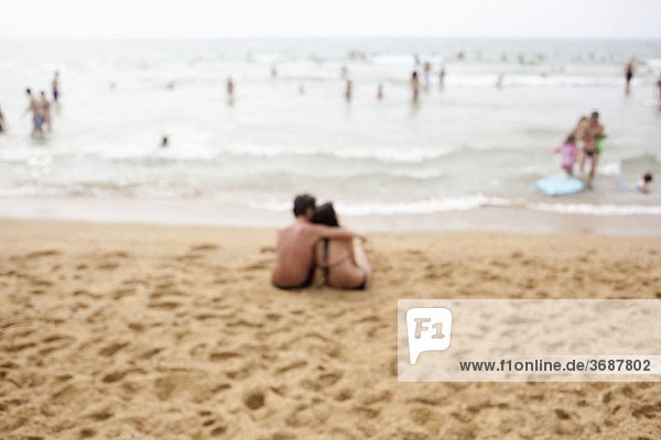 Ein Paar sitzt am Strand  defokussiert.