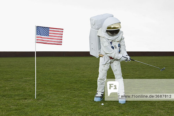 Ein Astronaut schwingt einen Golfschläger neben einer amerikanischen Flagge.