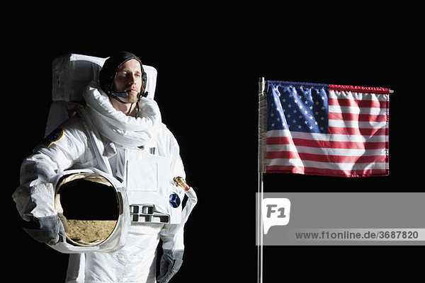 Ein Astronaut hält seinen Helm neben einer amerikanischen Flagge  Porträt