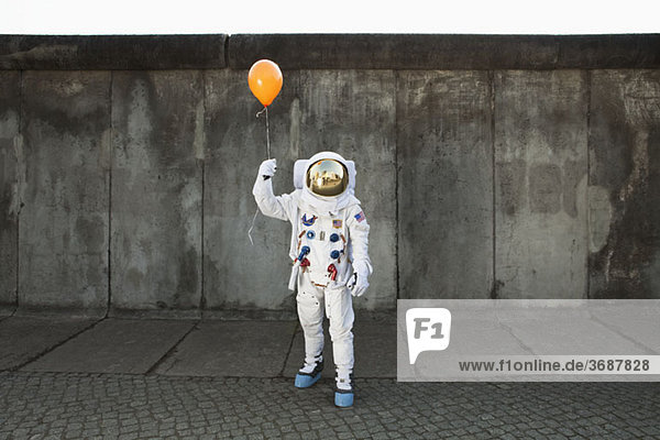Ein Astronaut auf einem Bürgersteig  der einen Ballon hält.