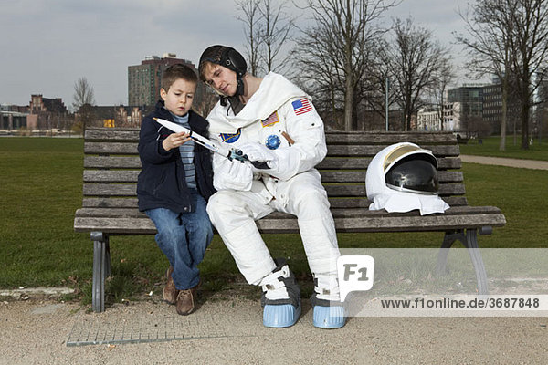 Ein Astronaut und ein Junge sitzen auf einer Parkbank und betrachten eine Modellrakete.