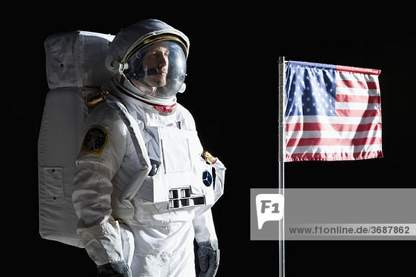 Ein Astronaut mit einem ernsten Ausdruck neben einer amerikanischen Flagge.