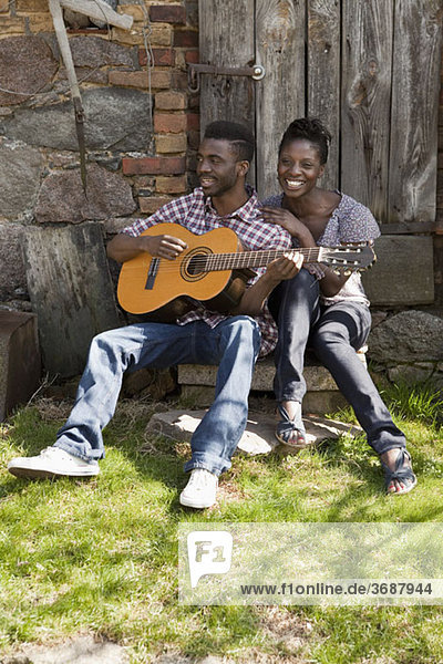 Ein Mann  der mit seiner Freundin eine Akustikgitarre spielt.