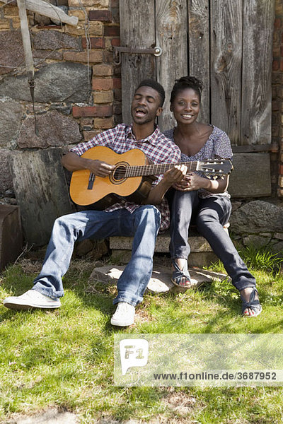 A man playing an acoustic guitar and singing with his girlfriend