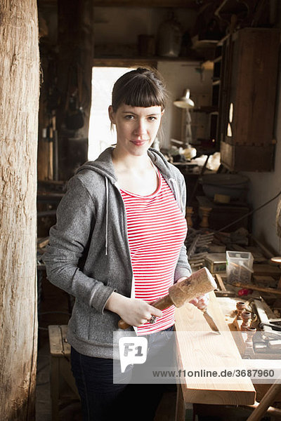 A woman in a workshop holding a chisel and mallet