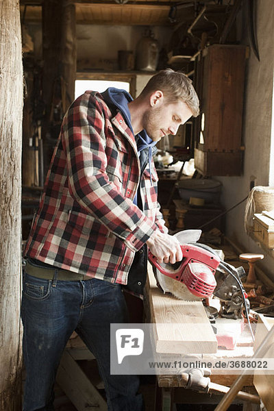 Ein Mann  der eine Kreissäge auf einem Brett in einer Werkstatt benutzt.