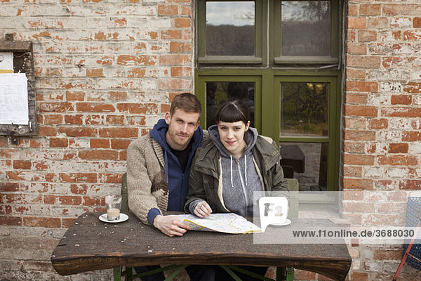 A couple with a map having lattes at an outdoor cafe