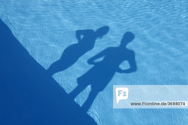 Schatten eines Mannes und einer Frau  die am Rande eines Schwimmbades stehen.
