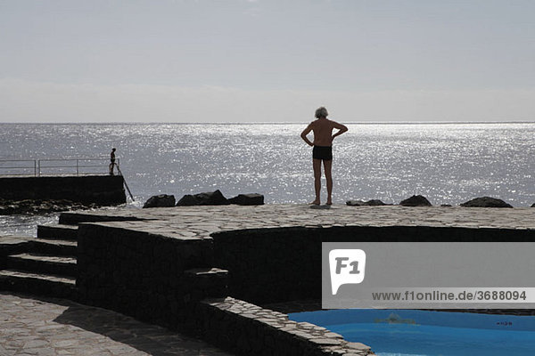 Ein Mann  der an einem Swimmingpool am Meer steht.