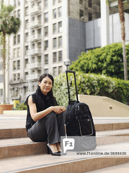 A businesswoman sitting on a step next to a rolling suitcase