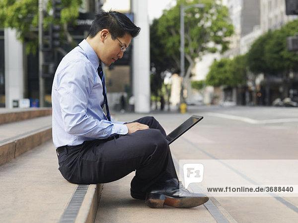 A businessman sitting cross-legged on some steps  using a laptop