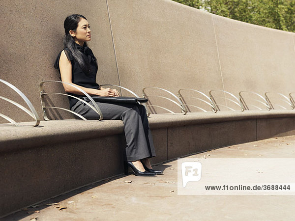 Eine Geschäftsfrau  die auf einer Zementbank sitzt.