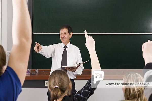 Ein Lehrer zeigt  während seine Schüler ihre Hände in einem Klassenzimmer erheben.